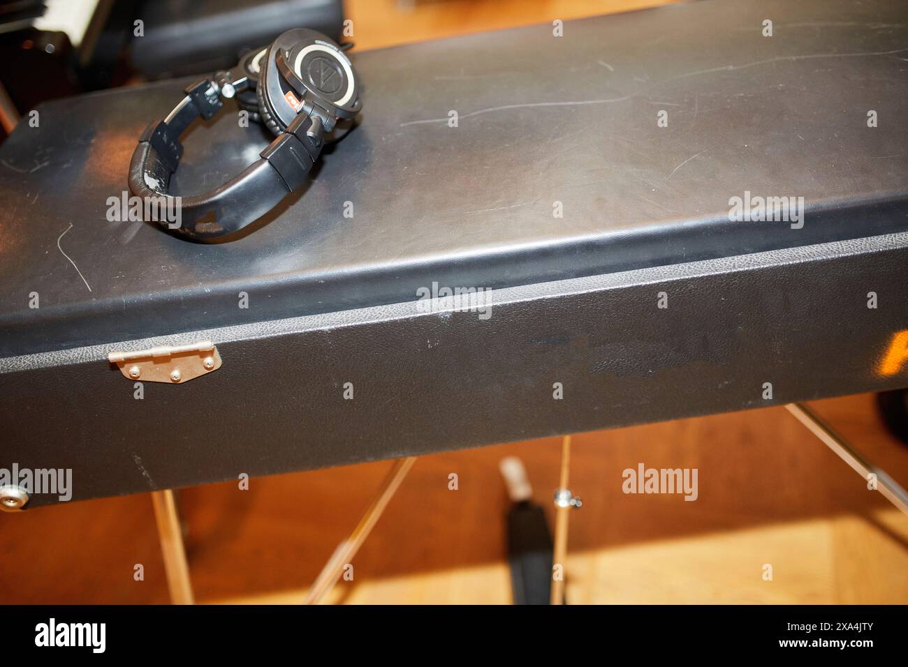 Eine schwarze Armbanduhr liegt auf einer strukturierten schwarzen Oberfläche, möglicherweise einem Gehäuse oder einer Bank, mit Holzmaserung und Metallelementen im Hintergrund. Stockfoto