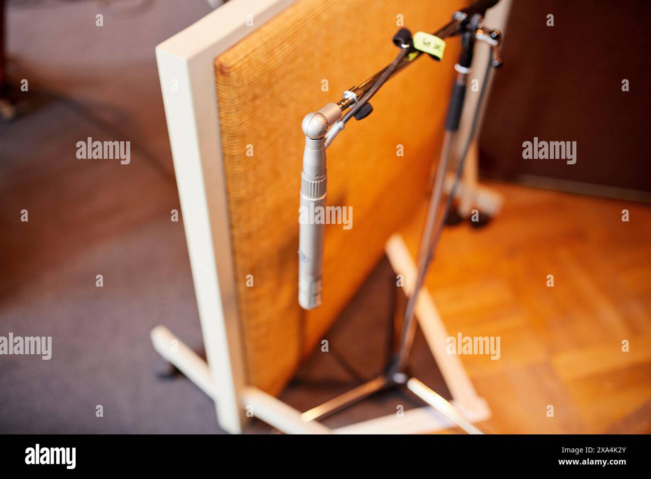 Nahaufnahme eines silbernen Mikrofons vor einem beigefarbenen Lautsprecherschrank auf Holzboden, mit selektivem Fokus und unscharfem Hintergrund. Stockfoto