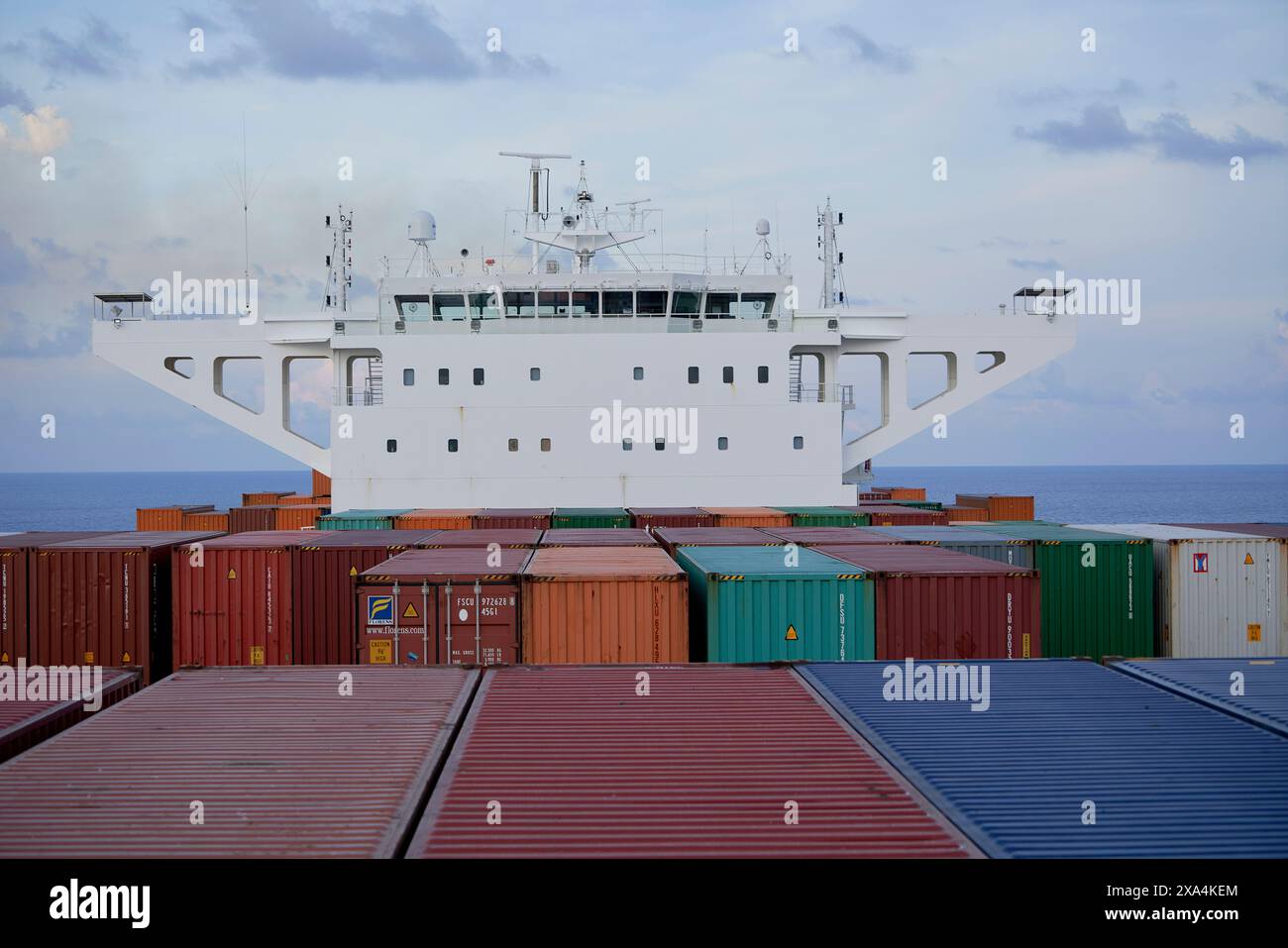 Ein großes Frachtschiff mit bunten Containern ist unter einem bewölkten Himmel zu sehen, dessen Brücke über den gestapelten Containern thront. Stockfoto