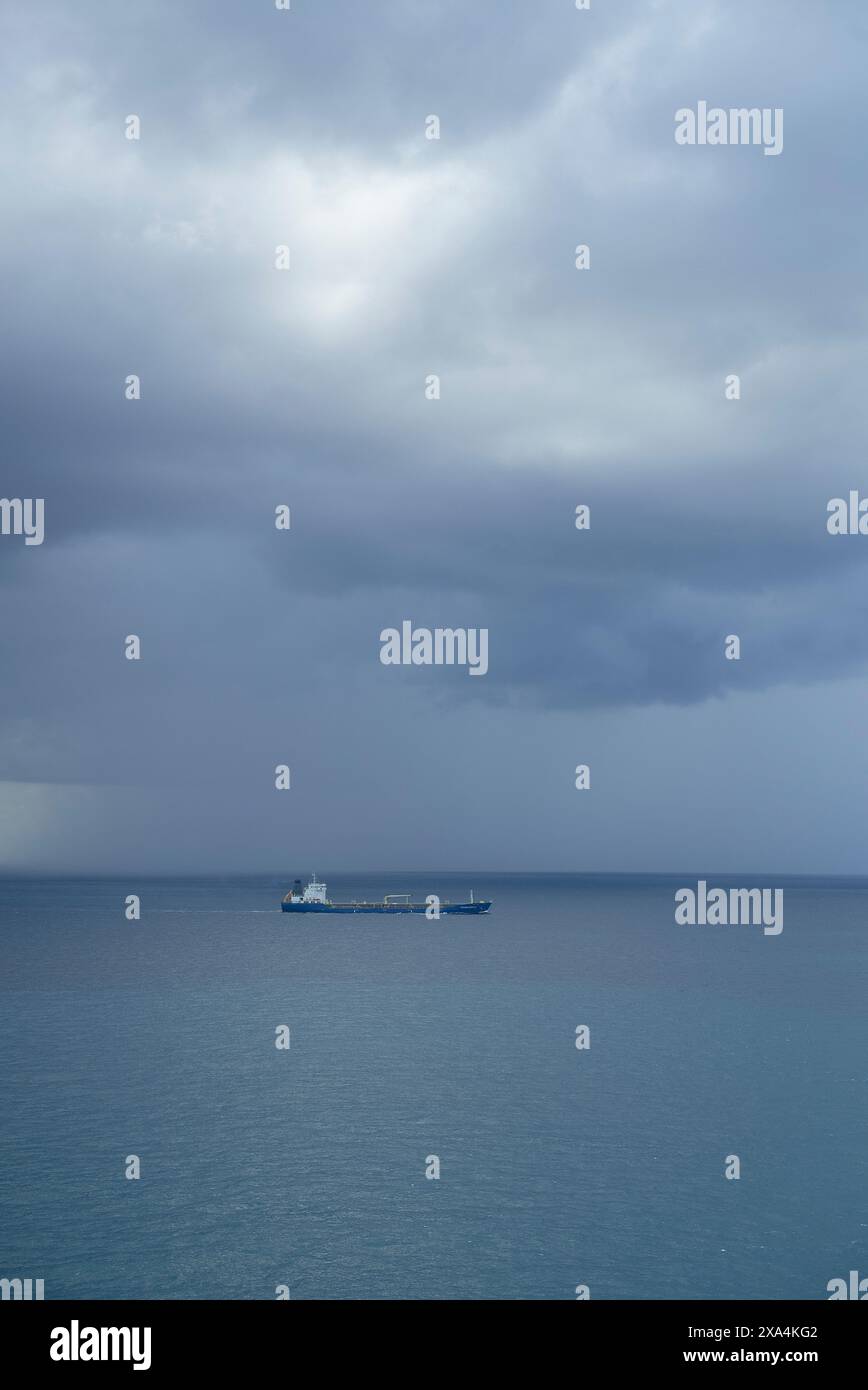 Ein einsames Schiff segelt auf einem riesigen Ozean unter einem dramatischen, stürmischen Himmel mit dunklen, bewölkten Wolken. Stockfoto