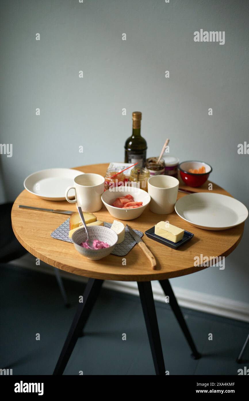 Ein übersichtlicher Frühstückstisch mit Schüsseln, Tellern, Tassen, einer Flasche und diversen Speisen in gemütlicher und einladender Atmosphäre. Stockfoto