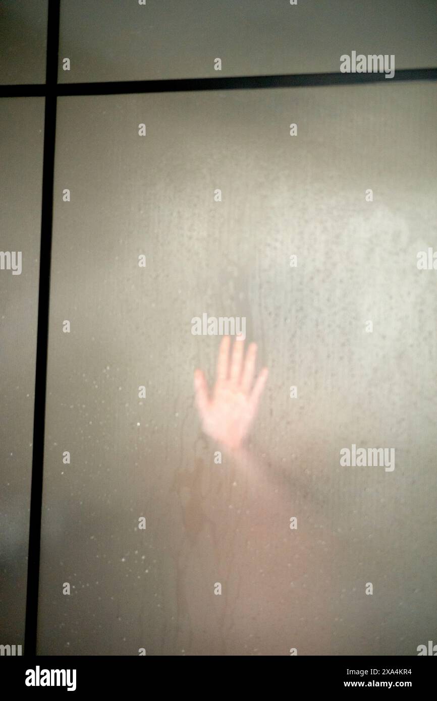 Die Hand einer Person wird gegen eine mattierte Glasscheibe gedrückt, wodurch eine Silhouette entsteht. Stockfoto