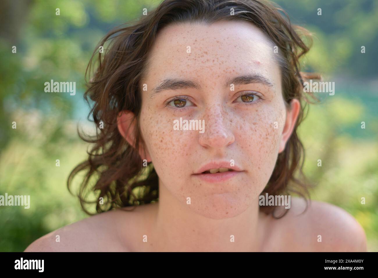 Nahaufnahme eines Porträts einer jungen Frau mit dunklen lockigen Haaren und einem Blick auf die Kamera, vor einem unscharfen grünen Hintergrund. Stockfoto