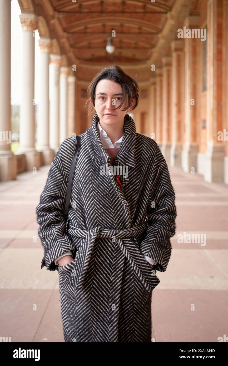 Eine Person steht selbstbewusst in einem großen Flur mit gewölbten Decken und trägt einen stilvollen Fischgrätmantel. Stockfoto