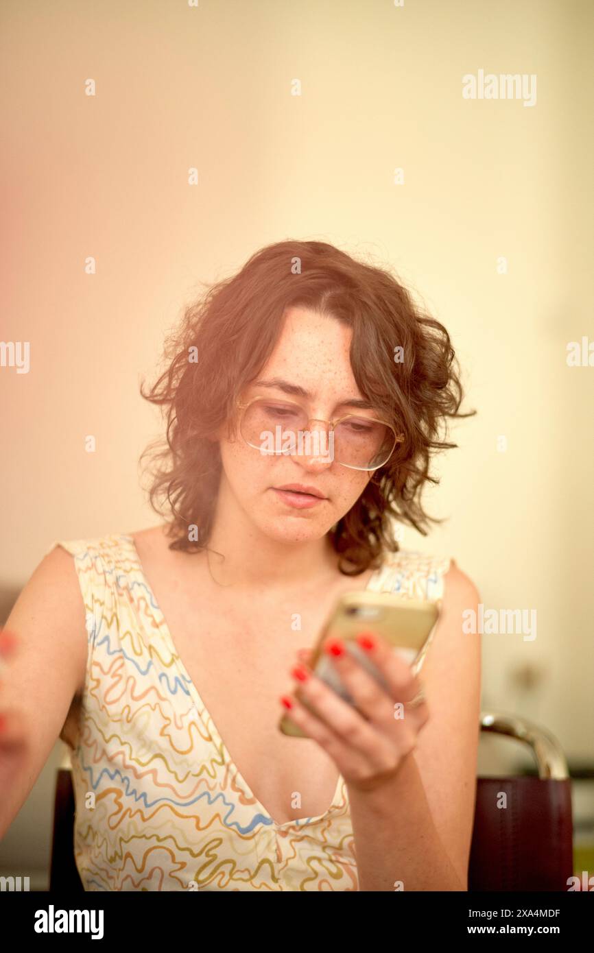 Eine Frau mit gewelltem Haar und Brille konzentriert sich auf ihr Smartphone. Stockfoto