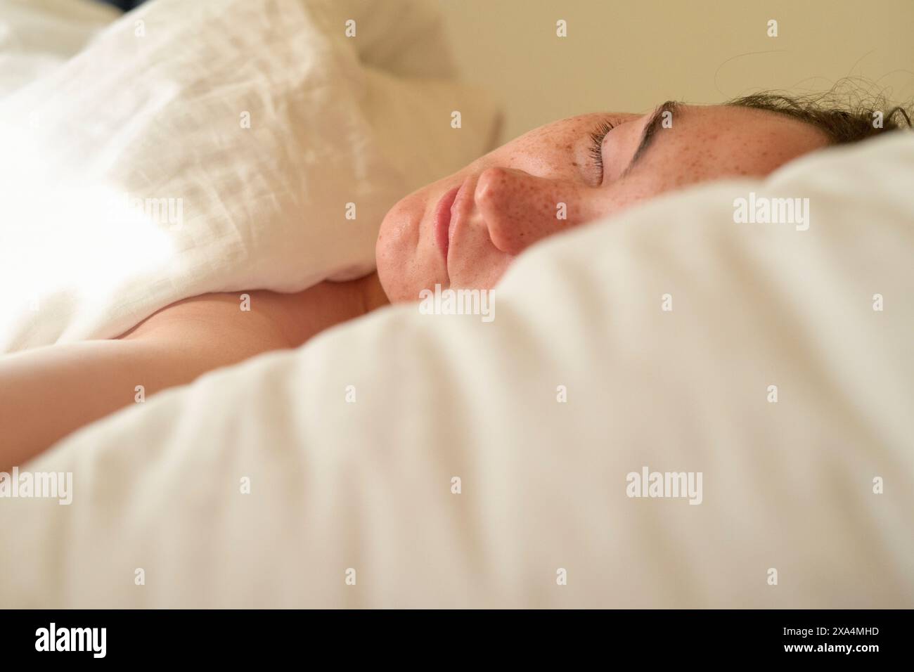 Ein Nahfoto einer jungen Frau, die friedlich im Bett liegt, mit dem Kopf auf einem Kissen, mit Sommersprossen auf der Wange und einem ruhigen Ausdruck. Stockfoto