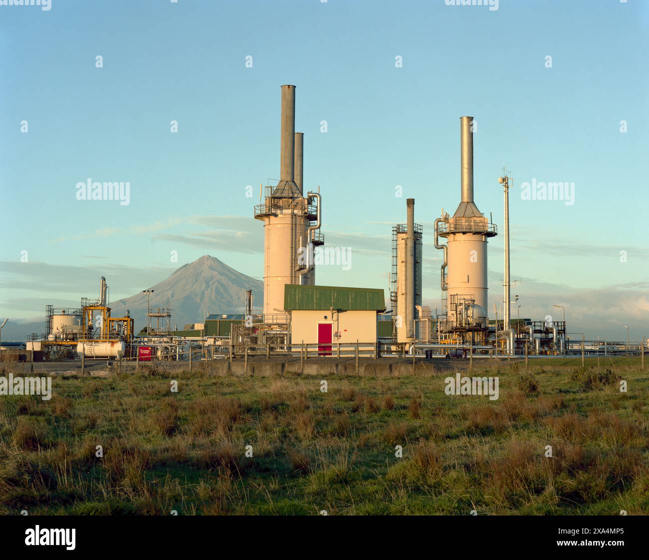 Industrielandschaft bei Sonnenuntergang auf Ackerland mit vulkanischem Berg im Hintergrund, Neuseeland Stockfoto