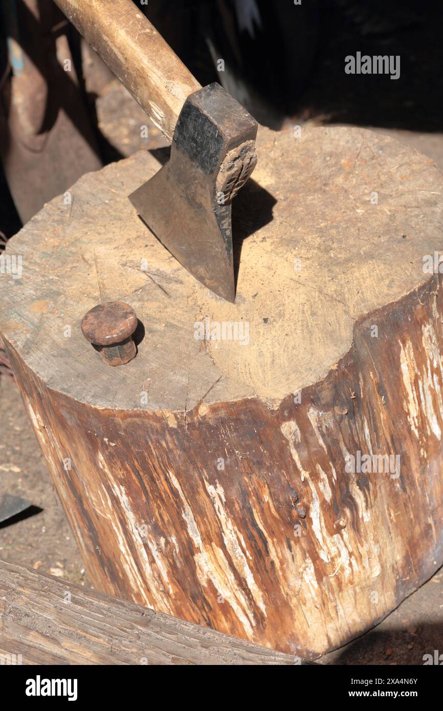 Die Axt ist in ein Holzdeck gehämmert. Als Nächstes ist ein Hammerbock zum Nieten einer Sense. Stockfoto