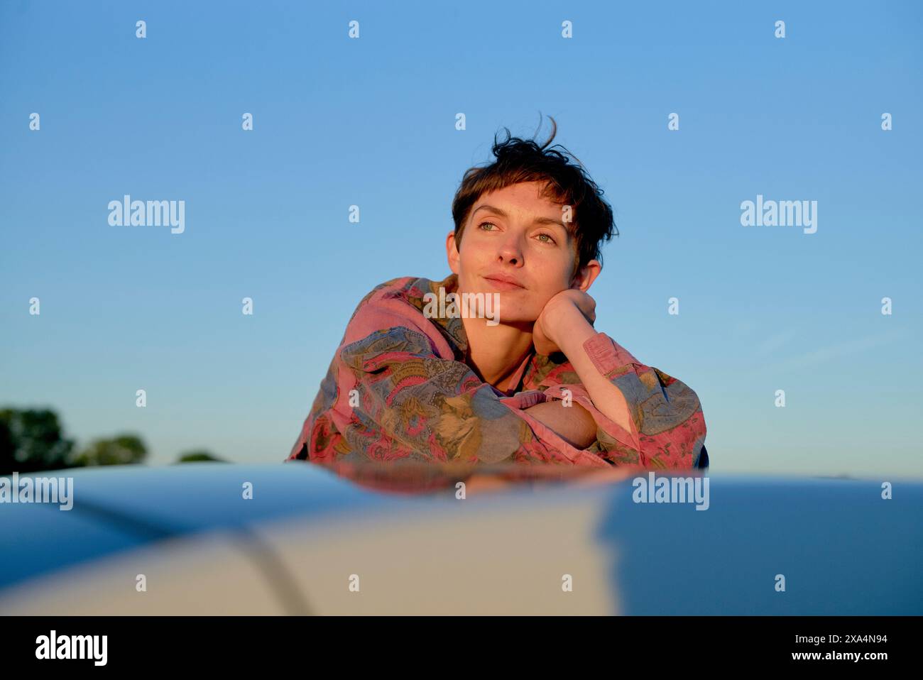 Eine Person blickt in die Ferne, legt ihr Kinn auf die Hand, mit dem Abendhimmel im Hintergrund. Stockfoto