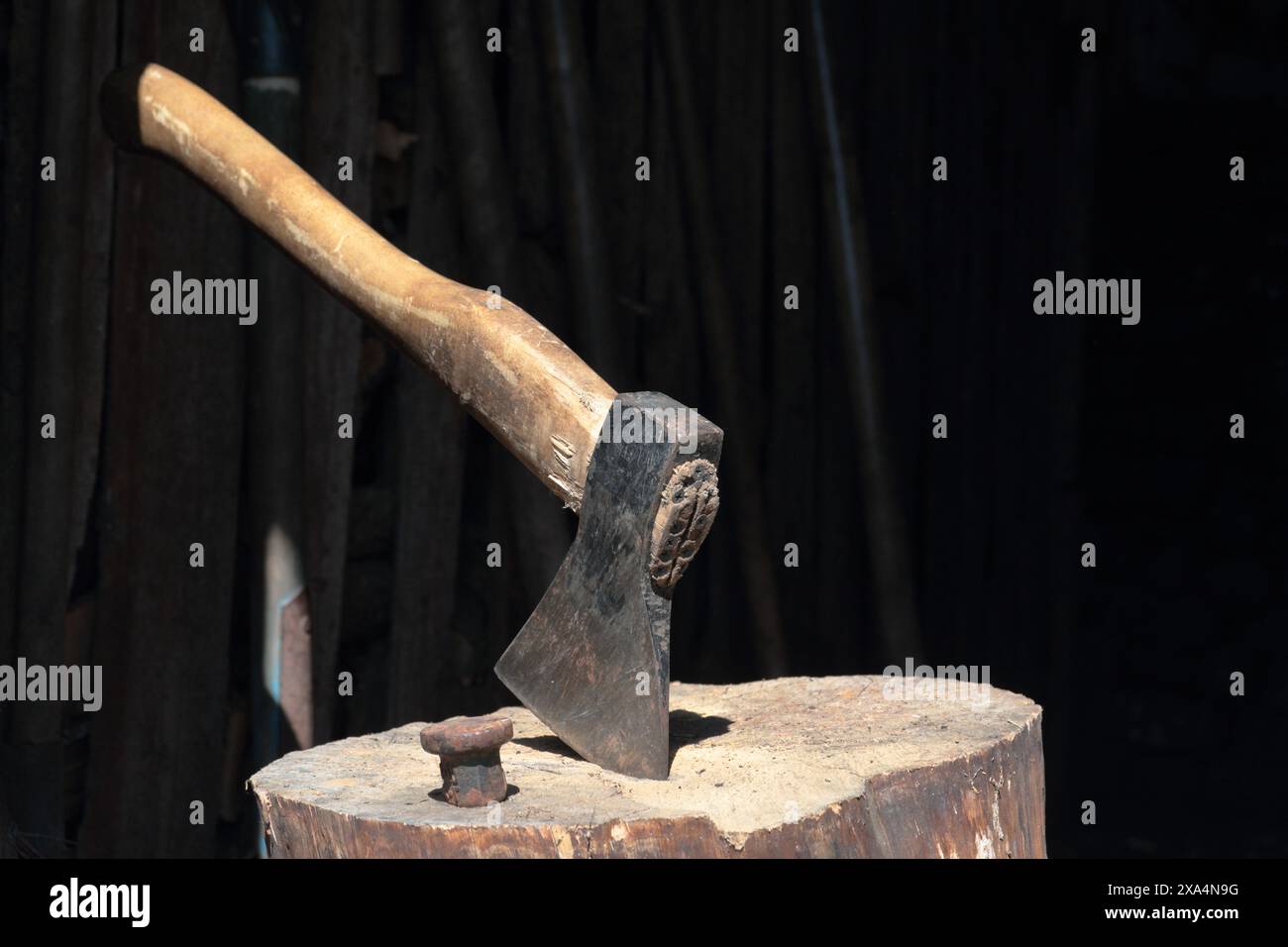 Die Axt ist in ein Holzdeck gehämmert. Als Nächstes ist ein Hammerbock zum Nieten einer Sense. Stockfoto