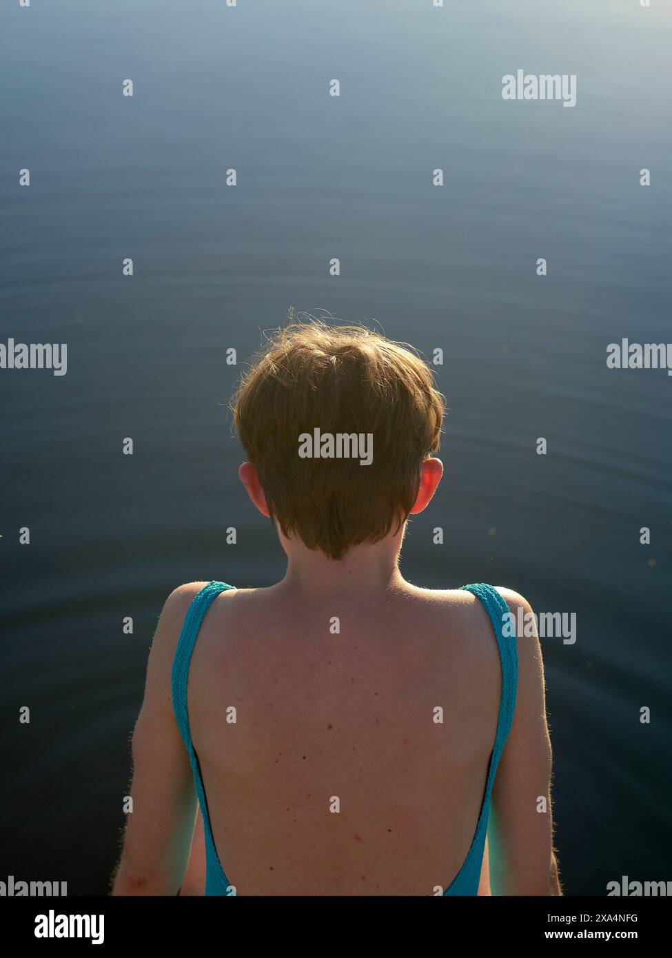 Eine junge Frau mit kurzen Haaren und blauen Badeanzügen steht vor einem ruhigen Gewässer. Stockfoto