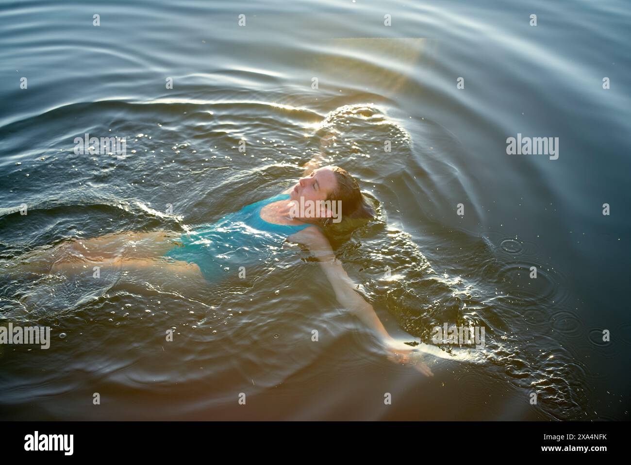 Eine junge Frau schwimmt in ruhigem Wasser mit Sonnenstrahlen auf der Oberfläche. Stockfoto