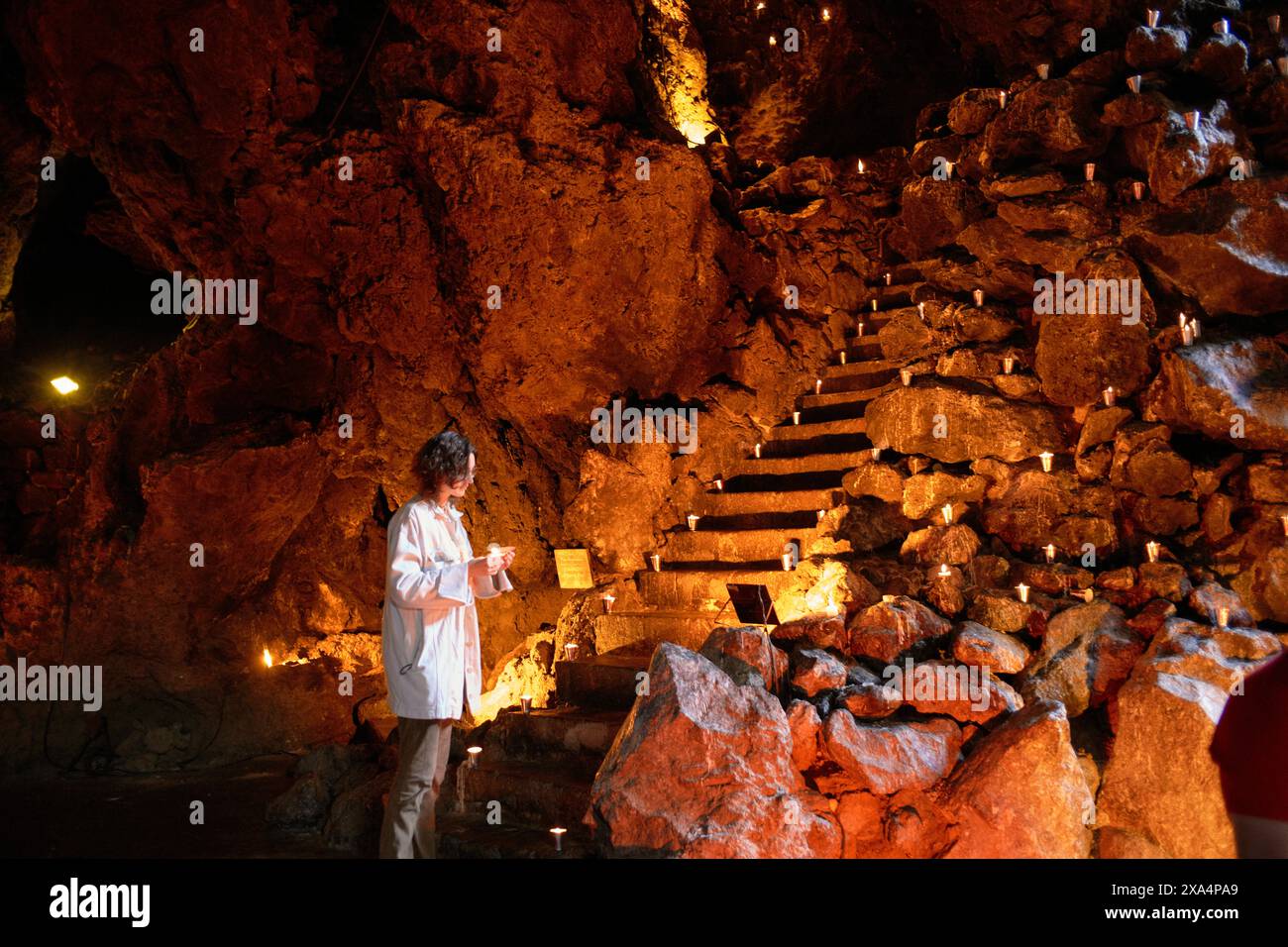 Eine junge Frau steht in einer schwach beleuchteten Höhle mit beleuchteten Stufen, die nach oben führen, und hält einen Notizblock. Stockfoto
