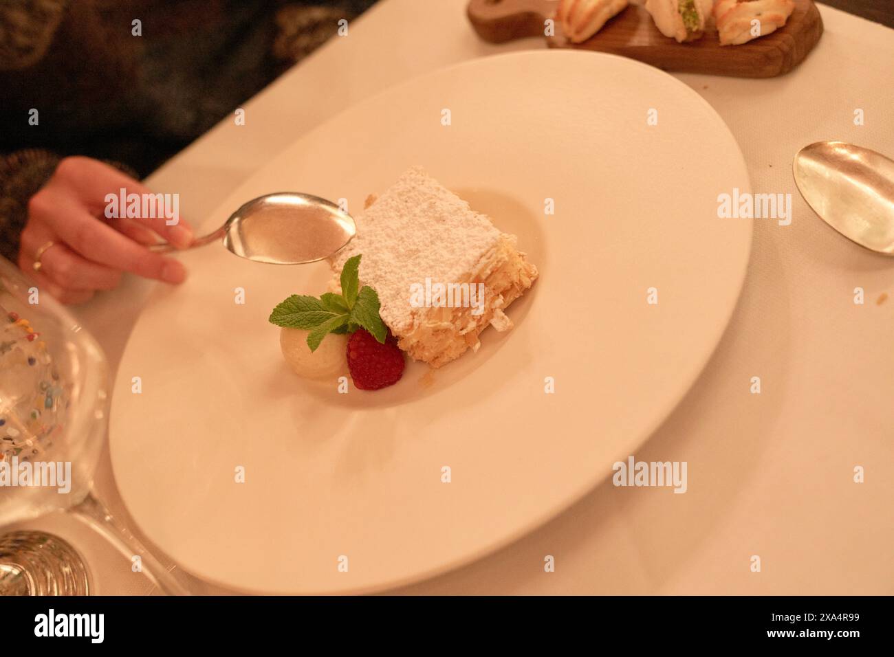 Elegantes Dessert auf einem weißen Teller, begleitet von einem Löffel aus Edelstahl, garniert mit Minze und Erdbeere Stockfoto