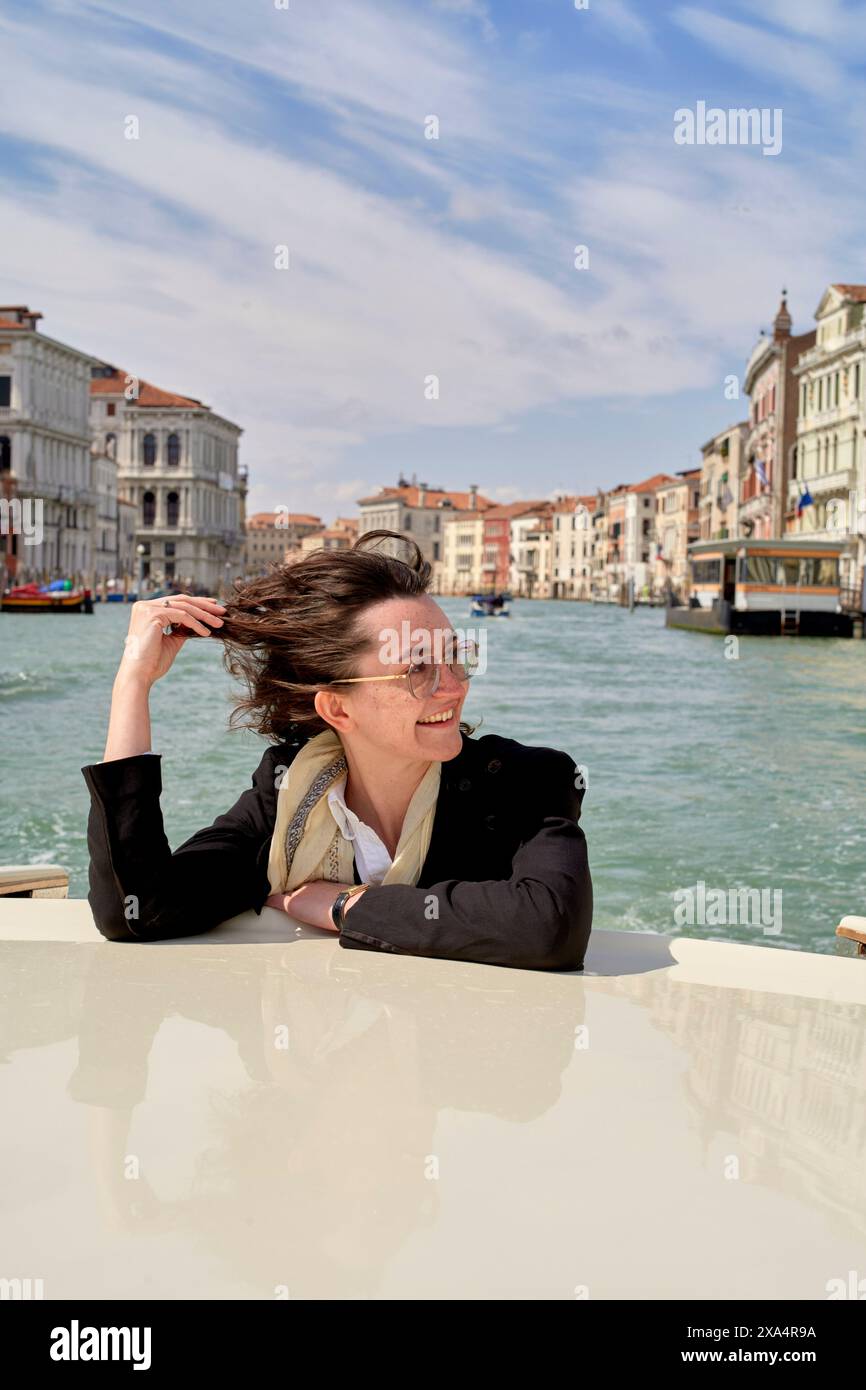Schicke Frau, die eine Bootsfahrt an einem hellen Tag mit Venedigs malerischen Kanälen im Hintergrund genießt. Stockfoto