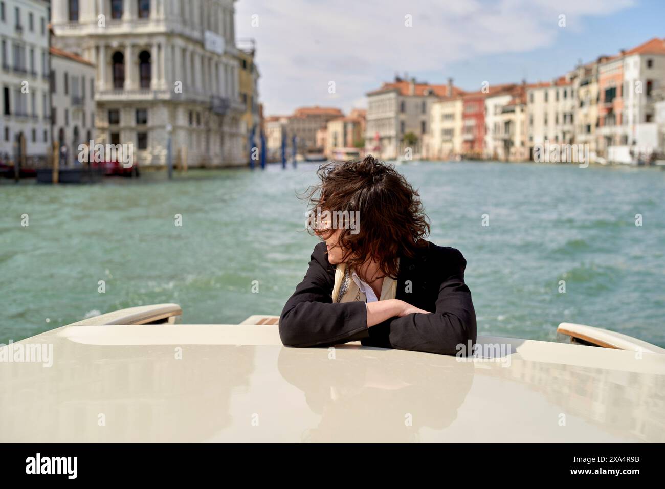 Windgepeitschte Touristen, die die Aussicht von einem Boot auf einem venezianischen Kanal genießen. Stockfoto