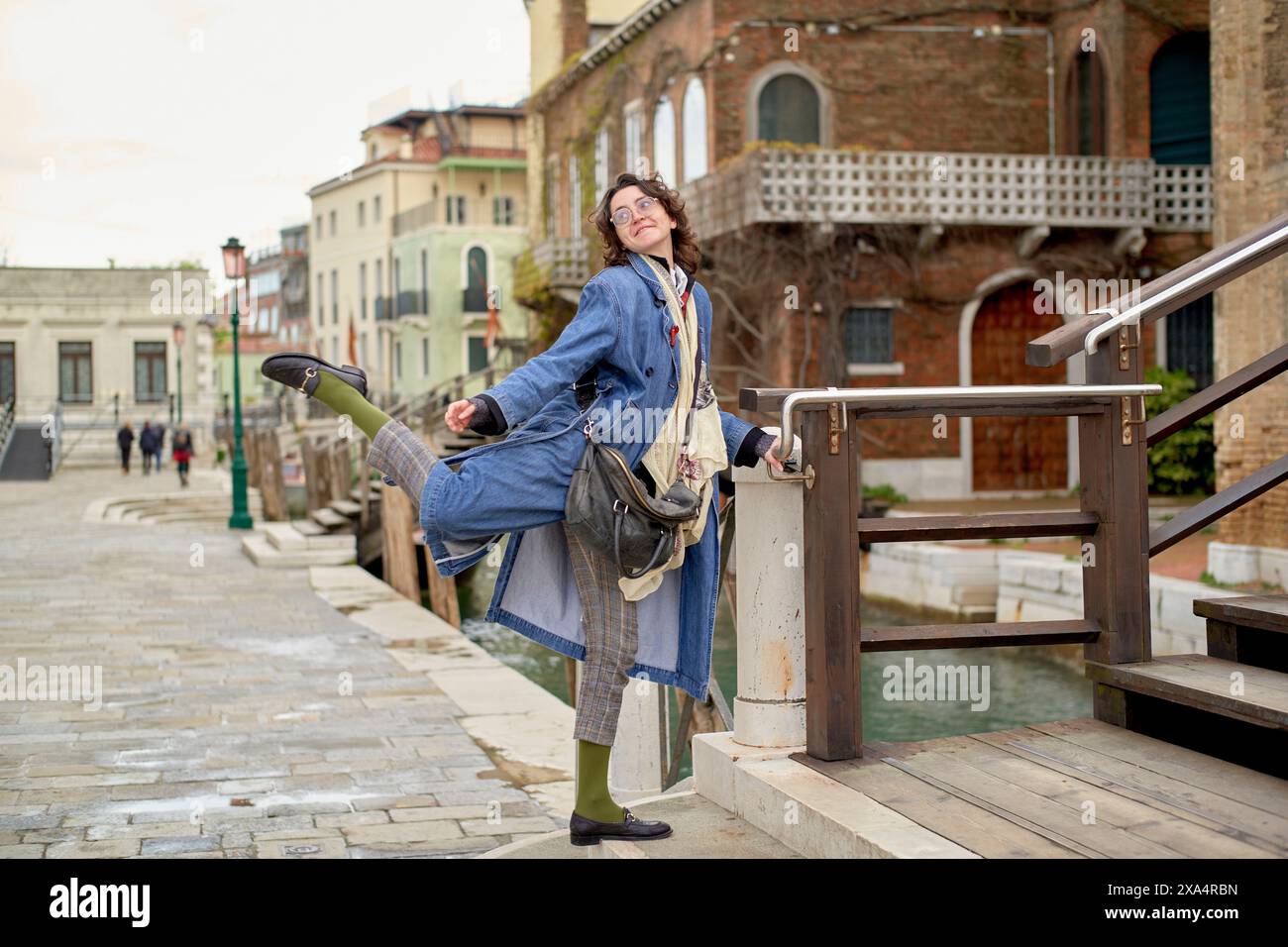 Fröhliche Frau tanzt auf einer Kanalbrücke von Venedig mit historischer Architektur im Hintergrund. Stockfoto