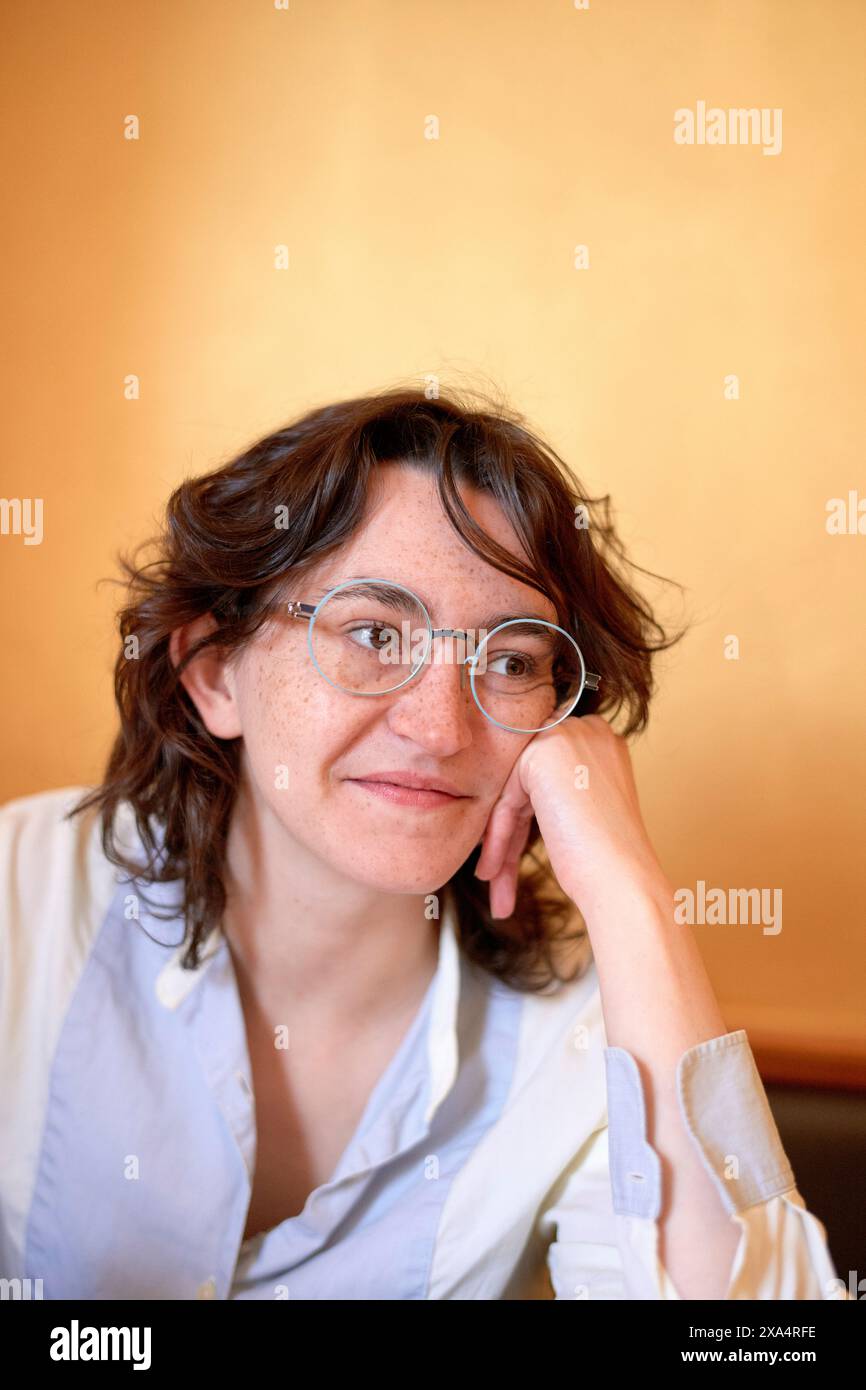 Lächelnde Frau mit einer Brille, die ihr Kinn auf der Hand vor einem warmen Hintergrund auflegt. Stockfoto