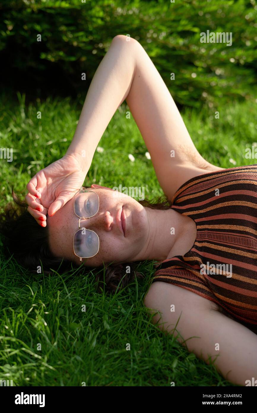 Frau, die sich auf dem Gras entspannt, mit Sonnenlicht, das durch ihre Hand über ihre Augen gefiltert wird. Stockfoto