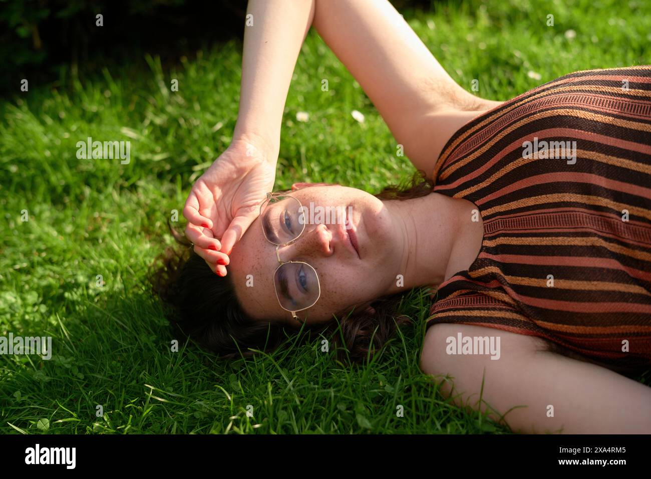 Frau, die sich im Sonnenlicht auf dem Gras mit einer Brille entspannt Stockfoto