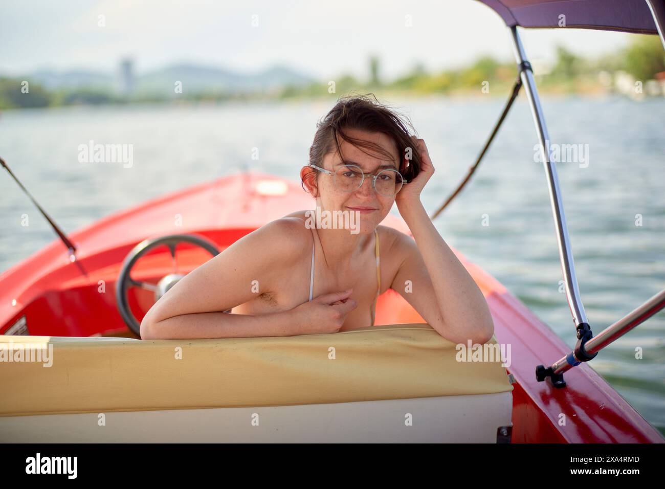 Eine junge Frau, die einen entspannten Moment auf einem roten Boot am See genießt. Stockfoto