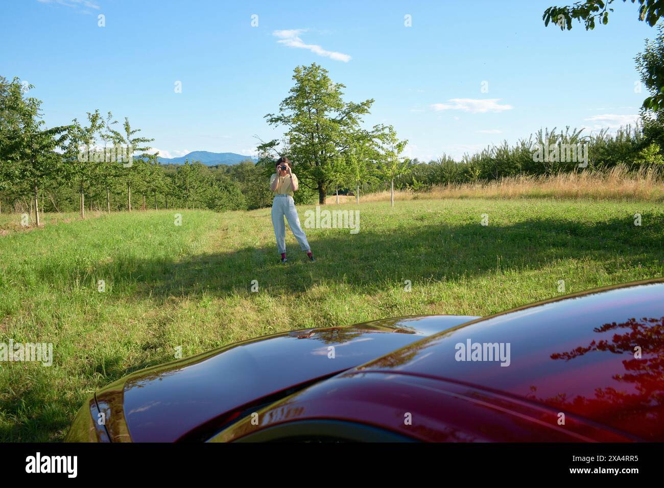 Fotograf, der die Schönheit der Natur neben einem roten Auto an einem sonnigen Tag auf dem Land festnimmt. Stockfoto