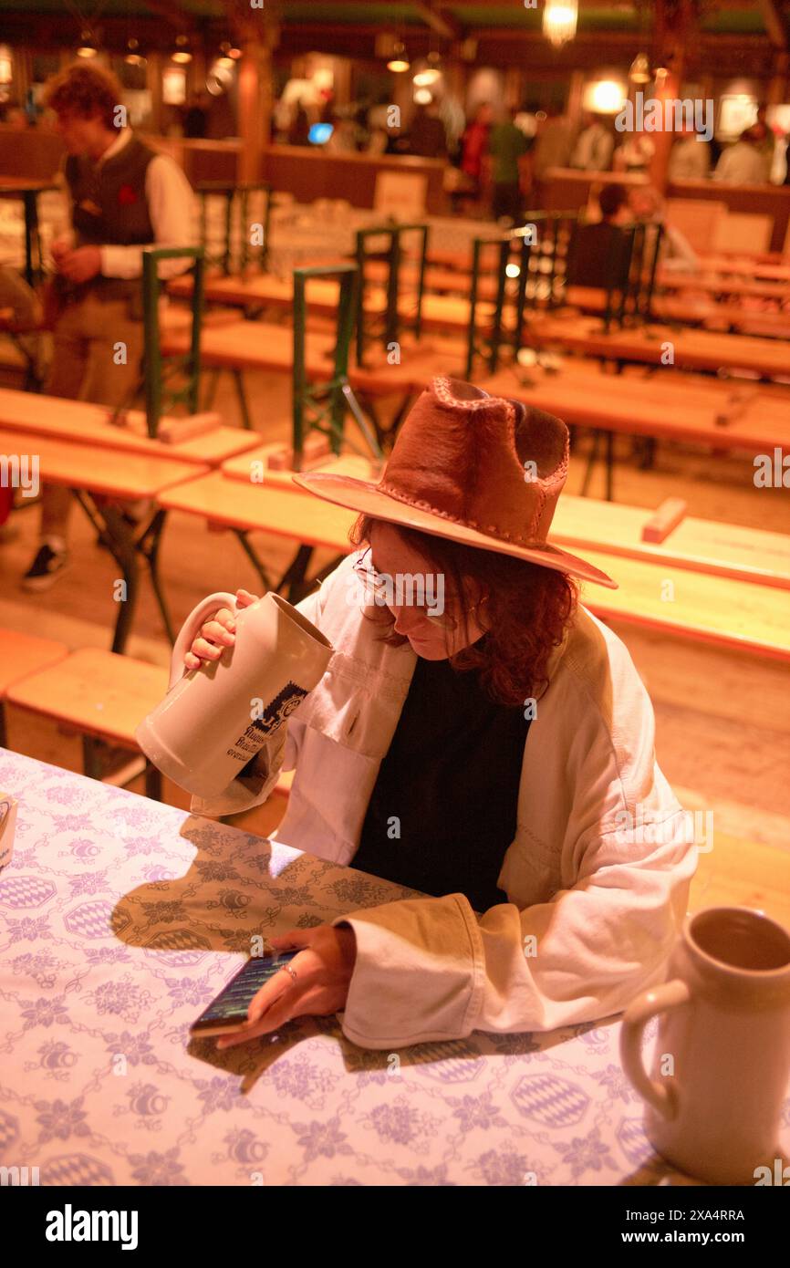 Frau in lässiger Kleidung mit Smartphone in einer warm beleuchteten Taverne. Stockfoto