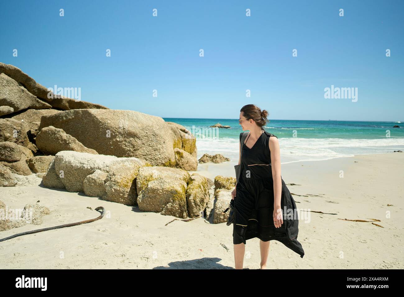 Frau, die an einem sonnigen Strand mit großen Felsen im Hintergrund läuft. Stockfoto