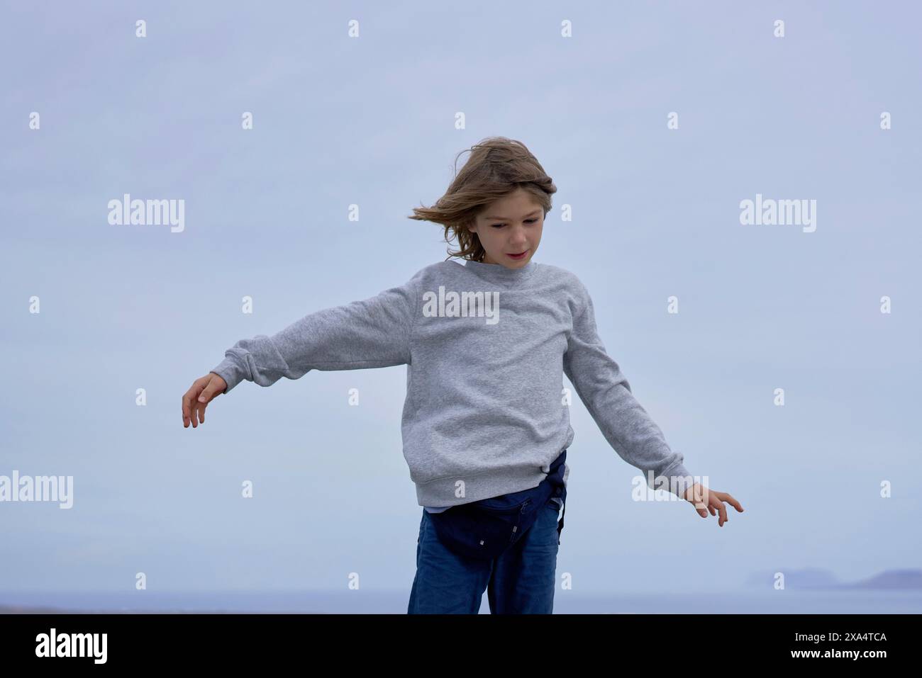 Ein kleines Kind in einem grauen Pullover und einer blauen Jeans genießt einen Moment des Spiels vor einem bewölkten Himmel. Stockfoto