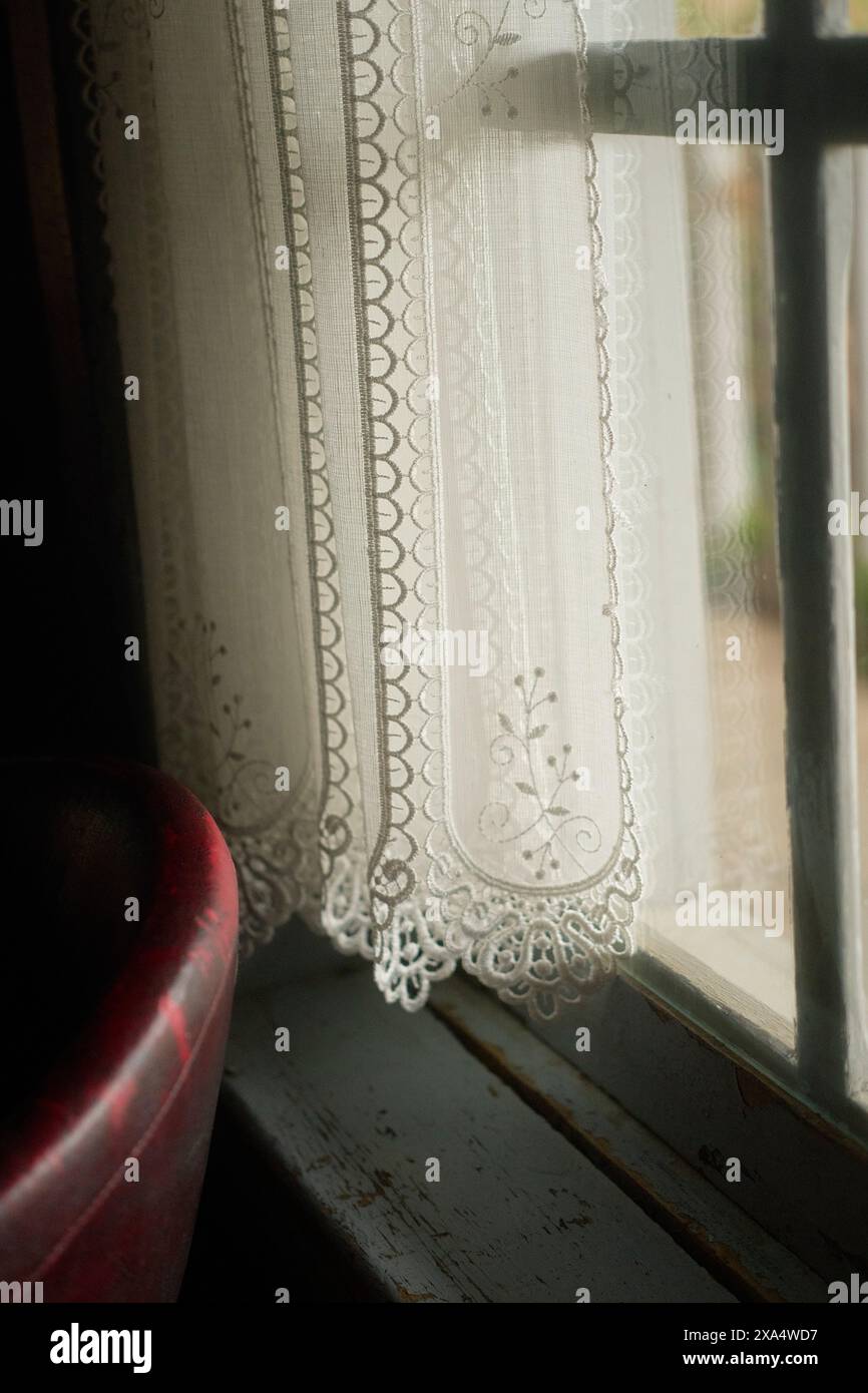 Weißer Spitzenvorhang mit kompliziertem Design hängt an einem Vintage-Holzfenster mit weichem Licht. Stockfoto