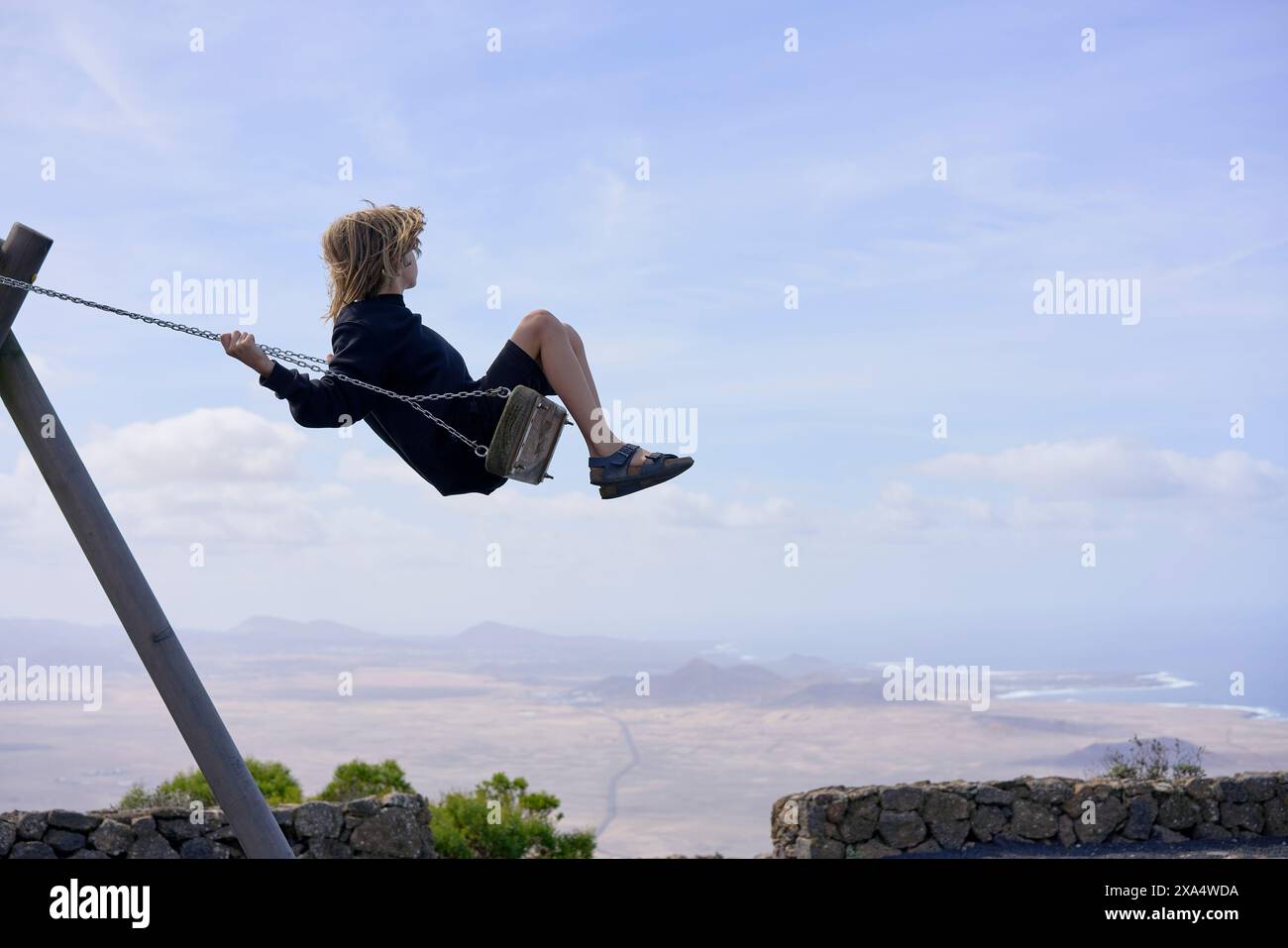 Frau schwingt hoch über der malerischen Landschaft mit Blick auf die Berge und die Küste. Stockfoto
