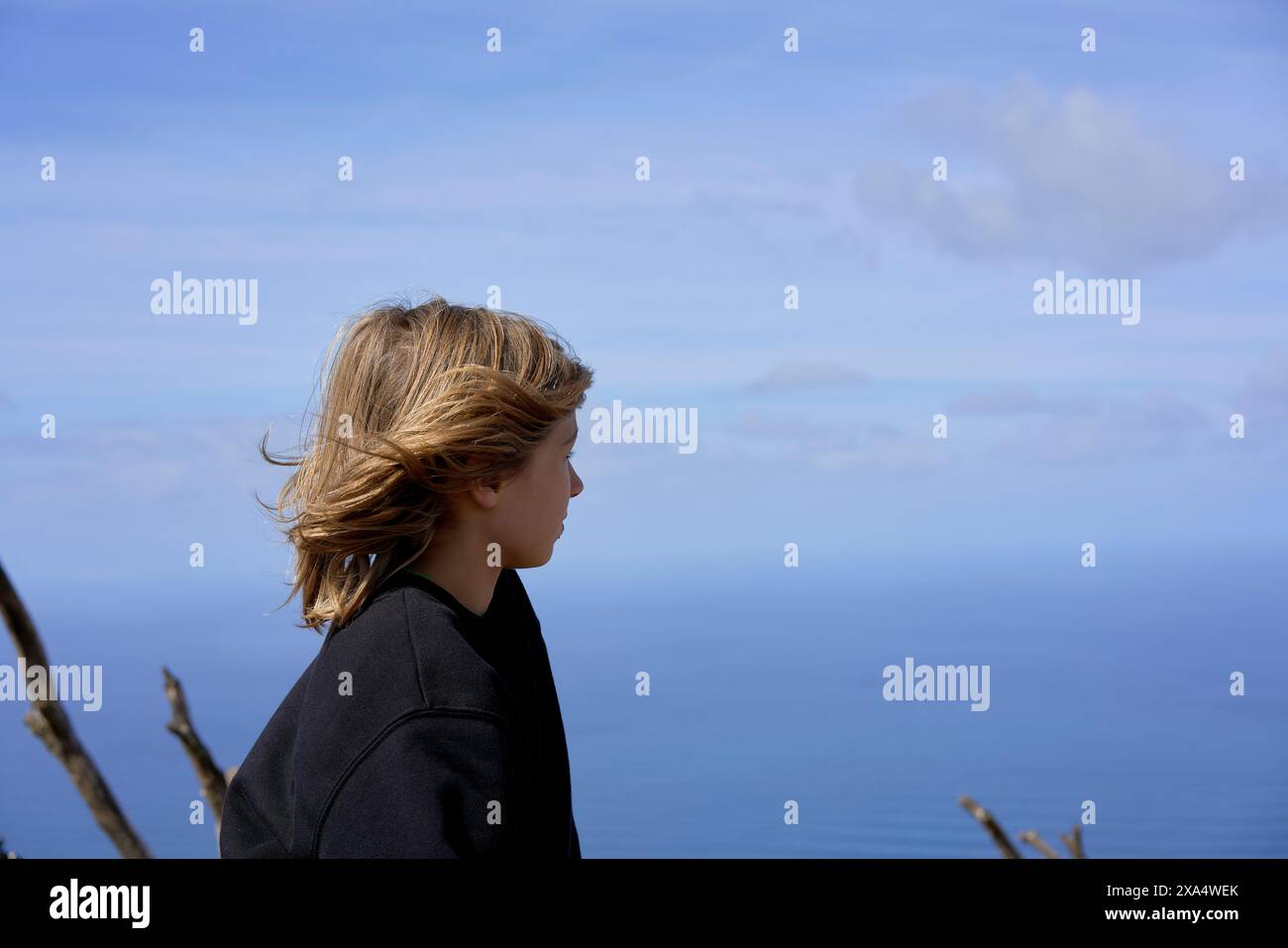 Frau mit blondem Haar, die an einem klaren Tag den Blick auf das Meer von einem hohen Aussichtspunkt genießt. Stockfoto