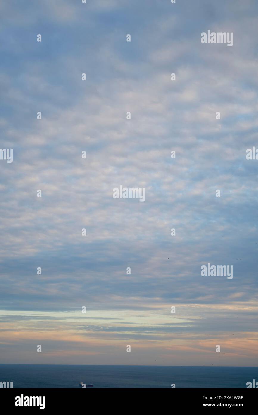 Sonnenuntergangshimmel mit Altocumulus-Wolken über einem ruhigen Ozean mit einem sichtbaren Schiff am Horizont. Stockfoto Sonnenuntergangshimmel mit Altocumulus-Wolken über einem ruhigen Ozean mit einem sichtbaren Schiff am Horizont. Stockfoto