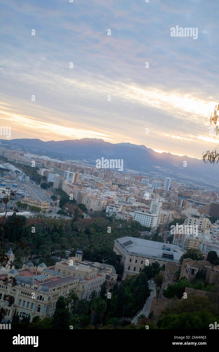 Blick auf den Sonnenuntergang über eine weitläufige Stadt mit Gebäuden und fernen Bergen unter einem pastellfarbenen Himmel. Stockfoto