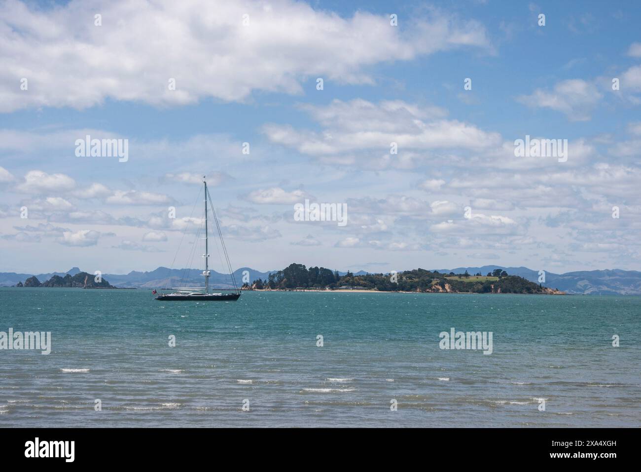 Segelbootfahrt in der Nähe einer Küsteninsel unter teilweise bewölktem Himmel. Stockfoto