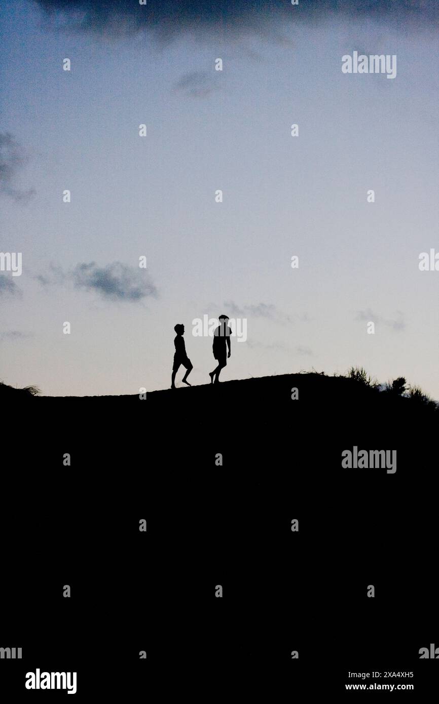 Silhouetten von zwei Individuen, die auf einem Hügel vor einem Abendhimmel spazieren. Stockfoto