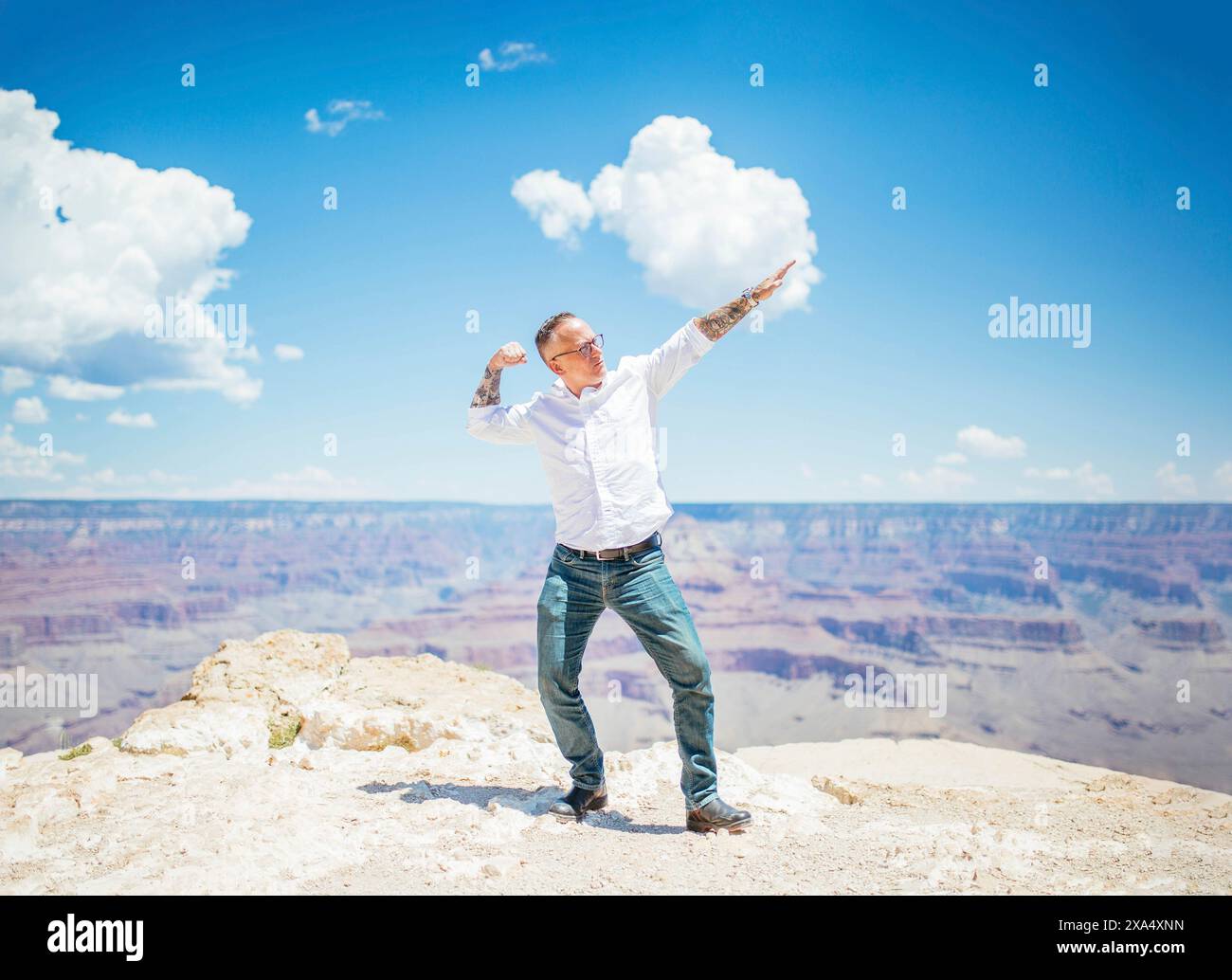 Der Mann streckt seine Arme weit offen am Rande des Grand Canyon unter einem klaren blauen Himmel. Stockfoto