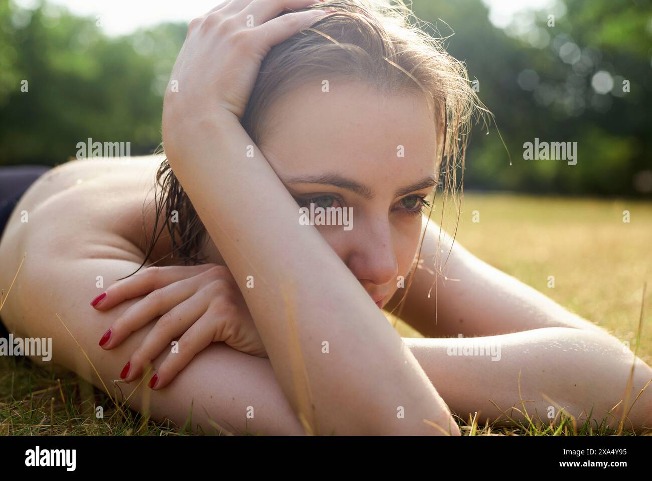 Nahaufnahme einer nachdenklichen Frau, die an einem sonnigen Tag auf dem Gras lag, mit dem Kopf auf den Armen. Stockfoto