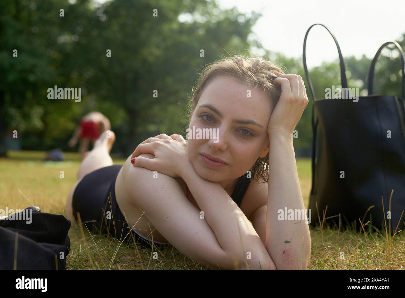 Frau, die sich an einem sonnigen Tag im Park auf dem Gras entspannt, mit einer Tragetasche in der Nähe. Stockfoto