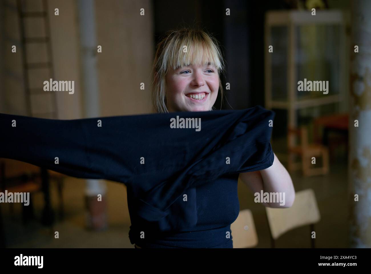 Lächelnde Frau mit blonden Haaren, die drinnen ein schwarzes Hemd anzieht. Stockfoto