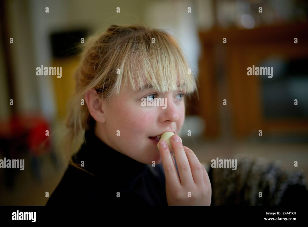 Eine Person mit blondem Haar isst eine Traube und blickt in die Ferne drinnen. Stockfoto