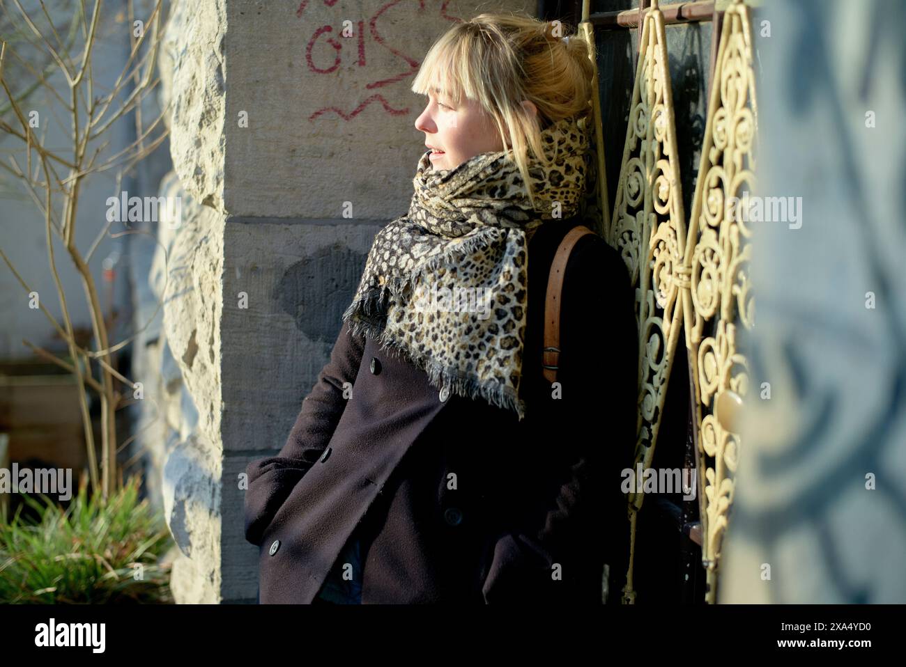 Frau, die an einem sonnigen Tag an einem schmiedeeisernen Tor steht, in einen Schal mit Leopardenmuster gewickelt. Stockfoto