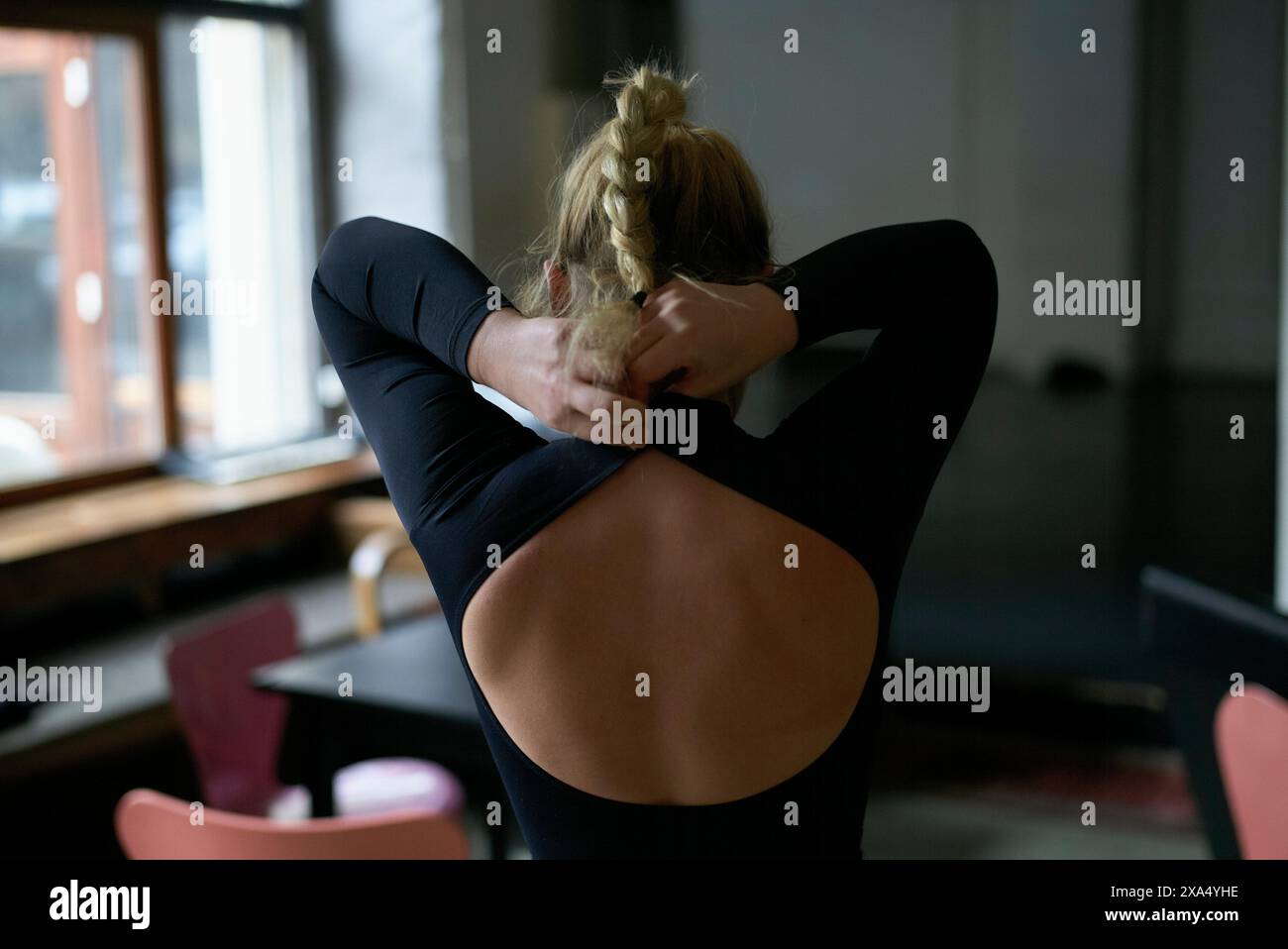 Eine Frau, die sich im Sitzen im oberen Rückenbereich in einem Innenbereich ausdehnt, wobei ihre Arme hinter ihrem Kopf reichen. Stockfoto