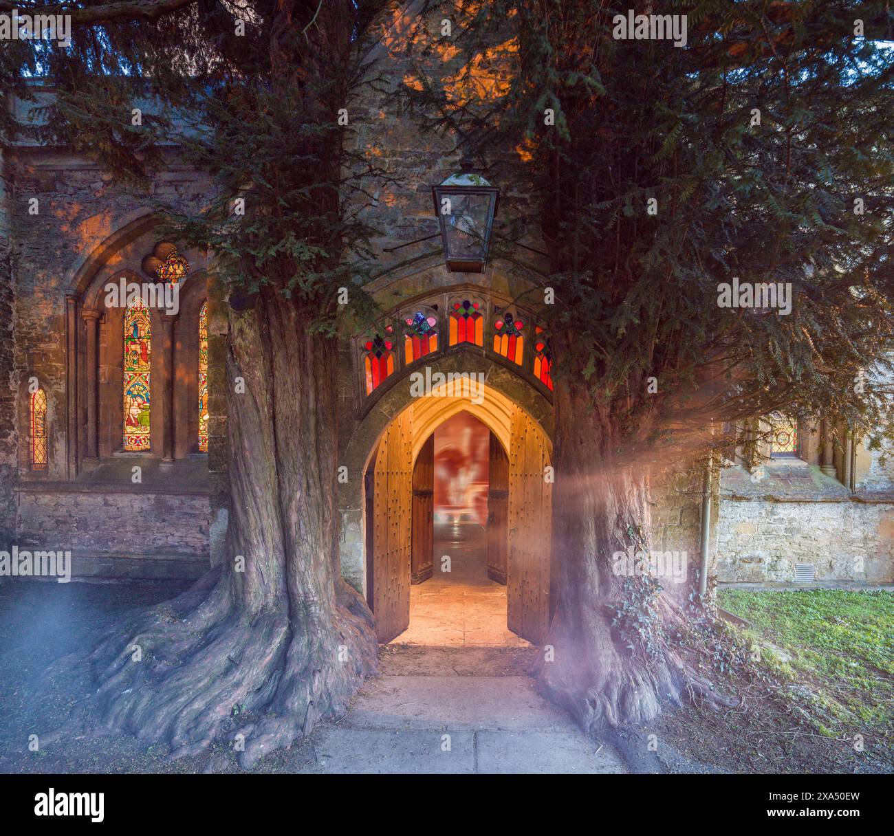 Gespenstische Figur, die in der Dämmerung durch den Bogengang einer alten Kirche mit beleuchteten Buntglasfenstern geht. St. Edwards Yew Stockfoto