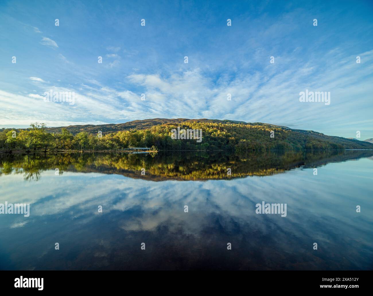 Ein ruhiger See, der den klaren blauen Himmel und herbstfarbene Bäume an einem ruhigen Tag reflektiert. Loch Lochy Stockfoto