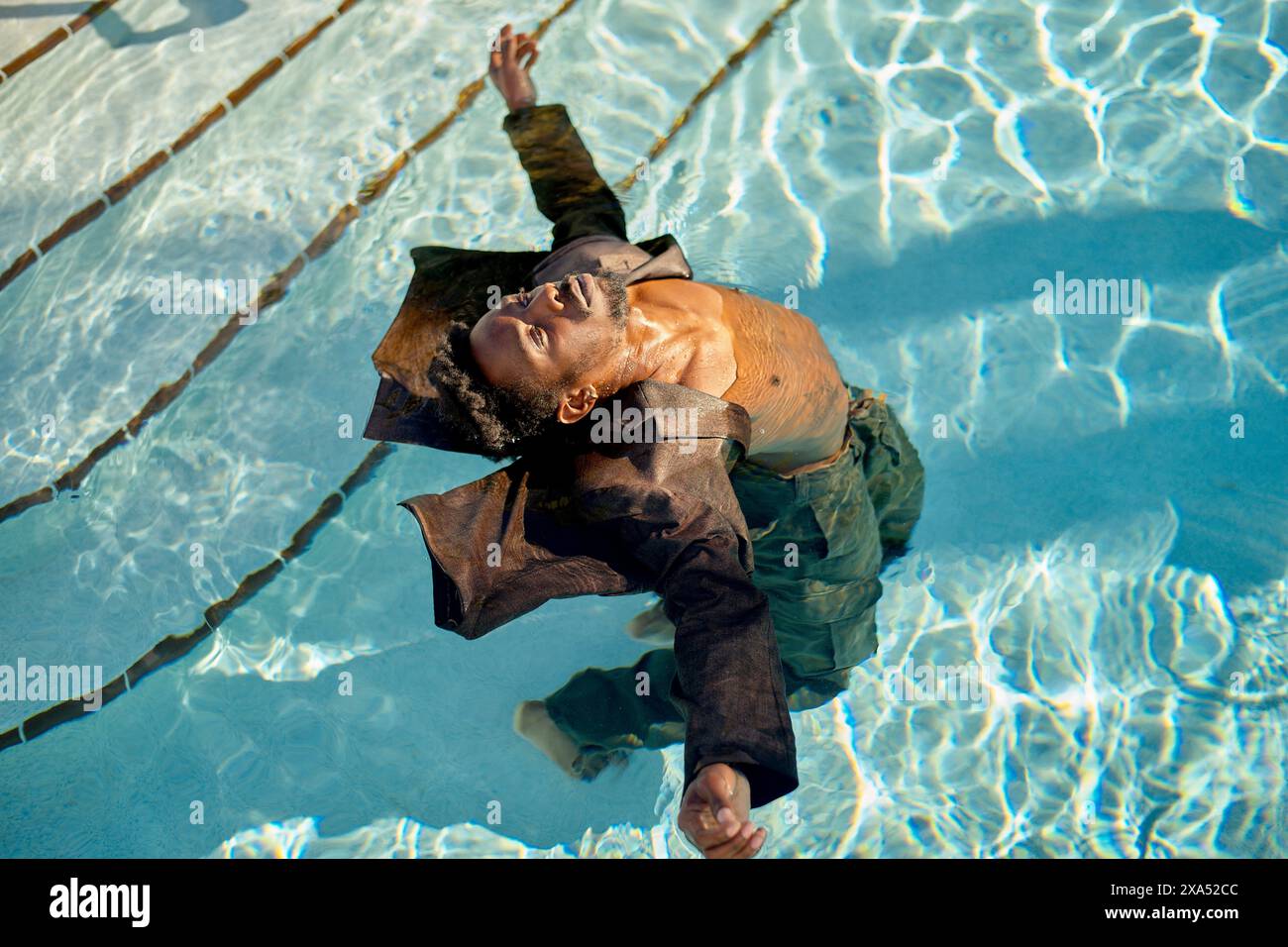 Mann schwimmt friedlich in einem klaren blauen Pool, seine Arme ausgestreckt und die Augen geschlossen in Entspannung. Stockfoto