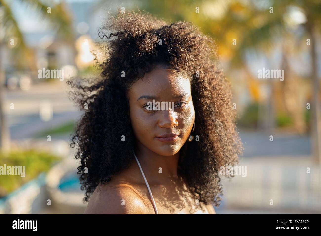 Porträt einer jungen Frau mit lockigem Haar, die draußen die goldene Stunde des Sonnenlichts genießt. Stockfoto