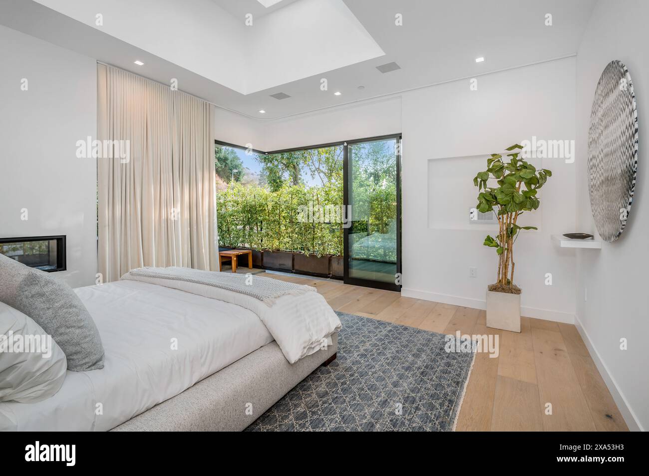 Ein modernes Schlafzimmer mit weißen Wänden, Kamin und hohen Fenstern Stockfoto