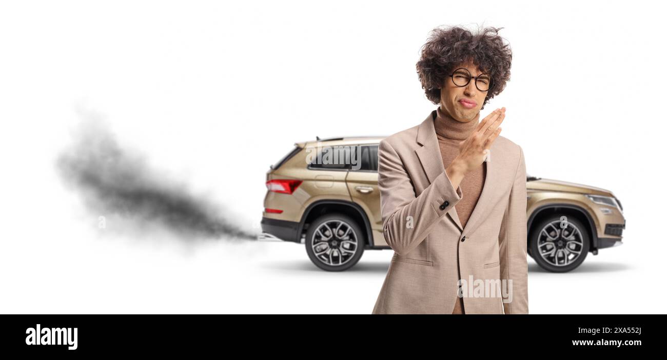 Wütender junger Mann vor einem Fahrzeug mit Abgasen, die gefährlich zu inhalieren sind, isoliert auf weißem Hintergrund Stockfoto