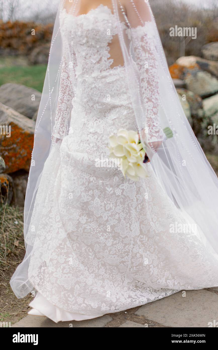 Braut schlendert auf einer Wiese mit weißem Blumenstrauß Stockfoto